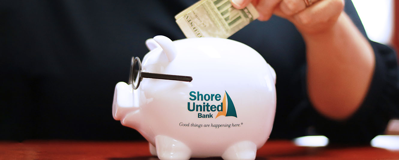 A lady wearing a navy blue shirt putting money into a Severn Savings Bank piggy bank.